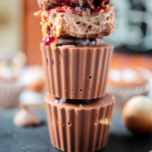 Closeup of stack of chocolate cups with nut butter and jelly. The top chocolate has a bite taken out to show the layers of nut butter and jelly.