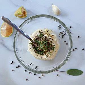 Glass bowl photographed from above with a sprinkle of sage and black pepper on garlic aioli