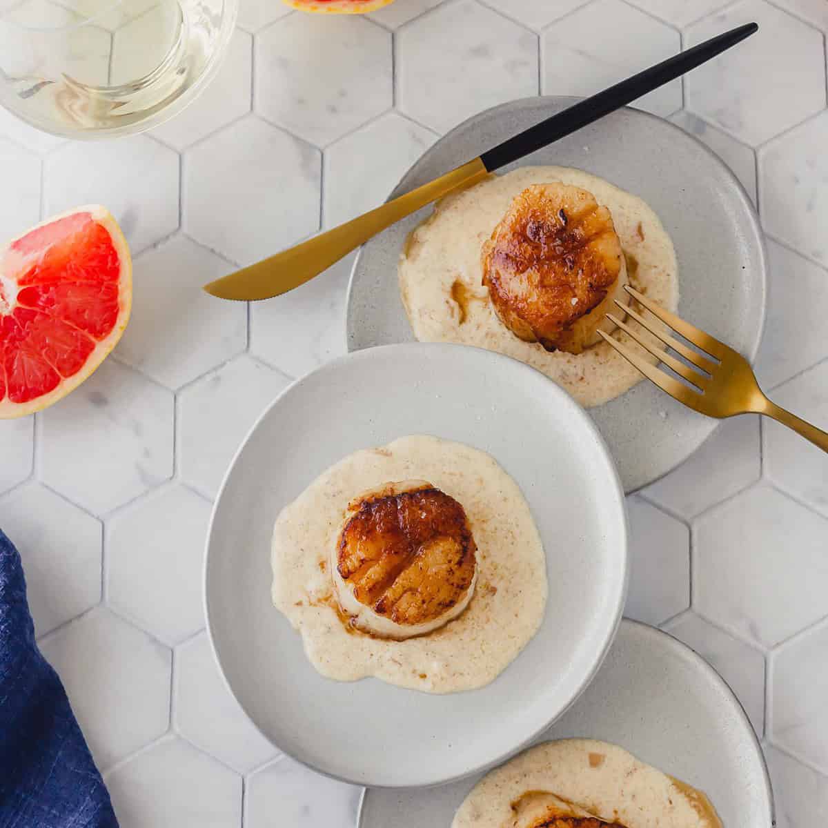 Three plates of seared scallops with grapefruit browned butter sauce arranged geometrically and styled by food photographer