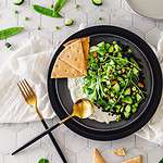 Fresh spring pea salad photographed from a birds eye view on a black plate with garnishes