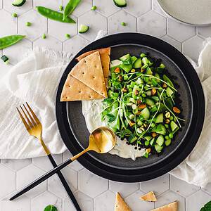Fresh spring pea salad photographed from a birds eye view on a black plate with garnishes
