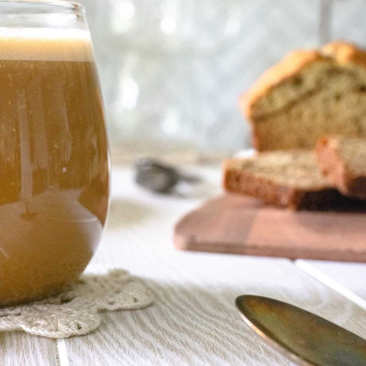 Banana Bread latte in clear glass cup with banana bread in background