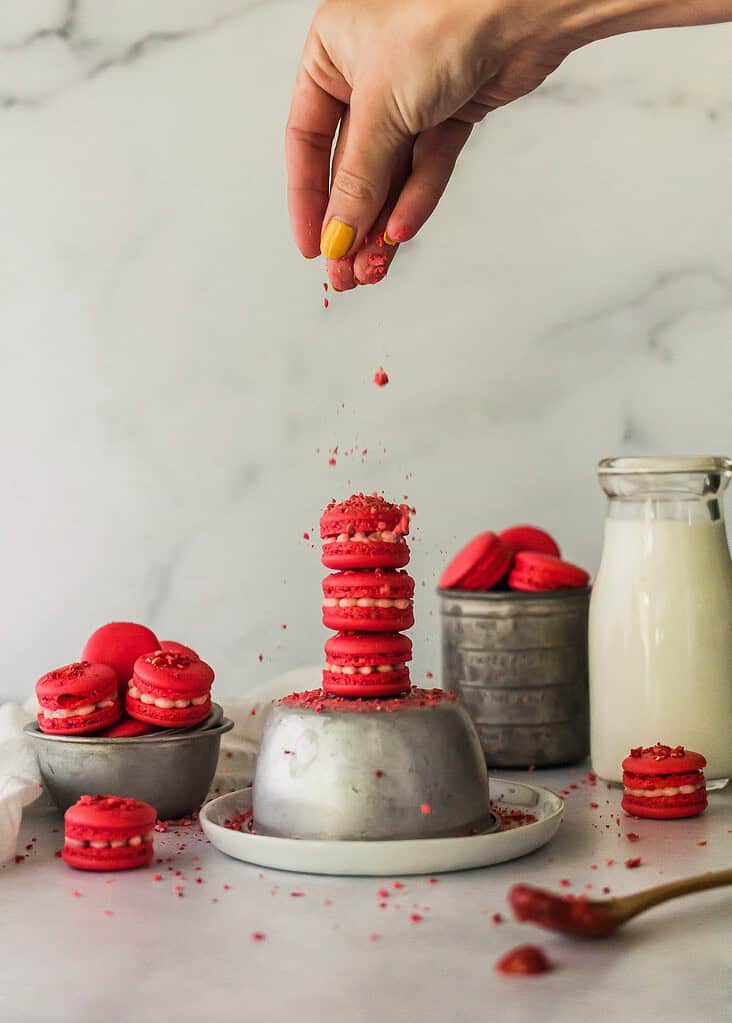 mini macarons on silver baking cups with milk in background and hand dropping strawberry pieces