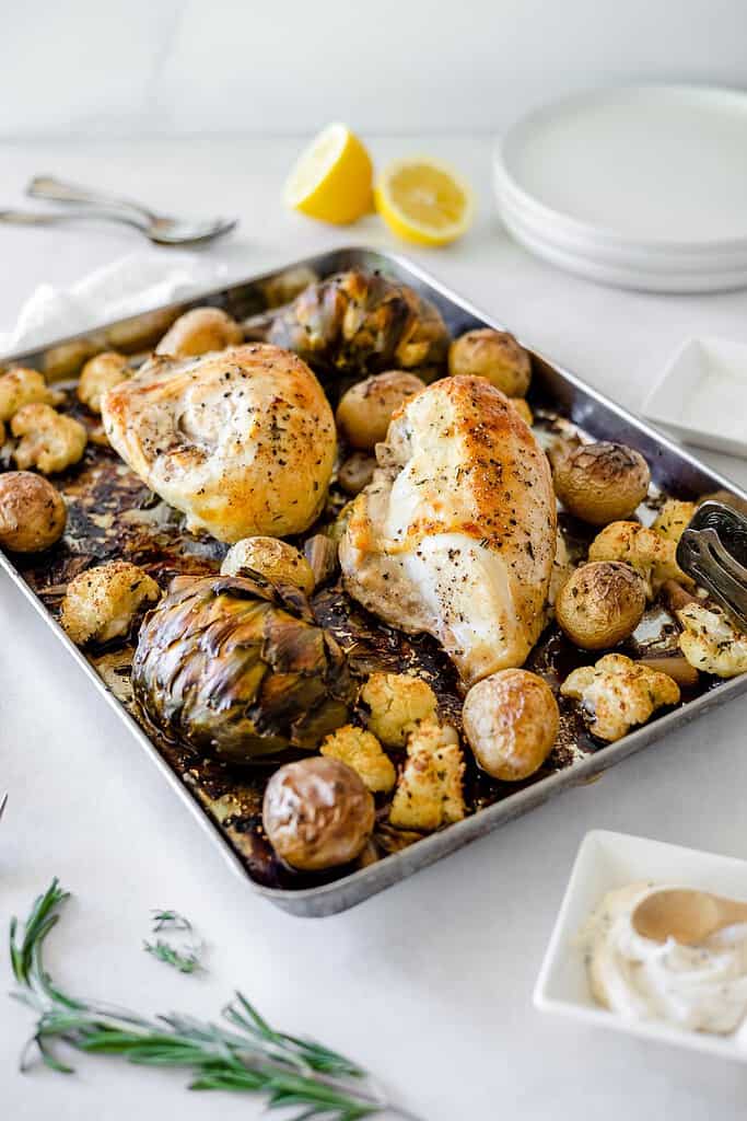 chicken and veggies on a sheet pan with lemon behind